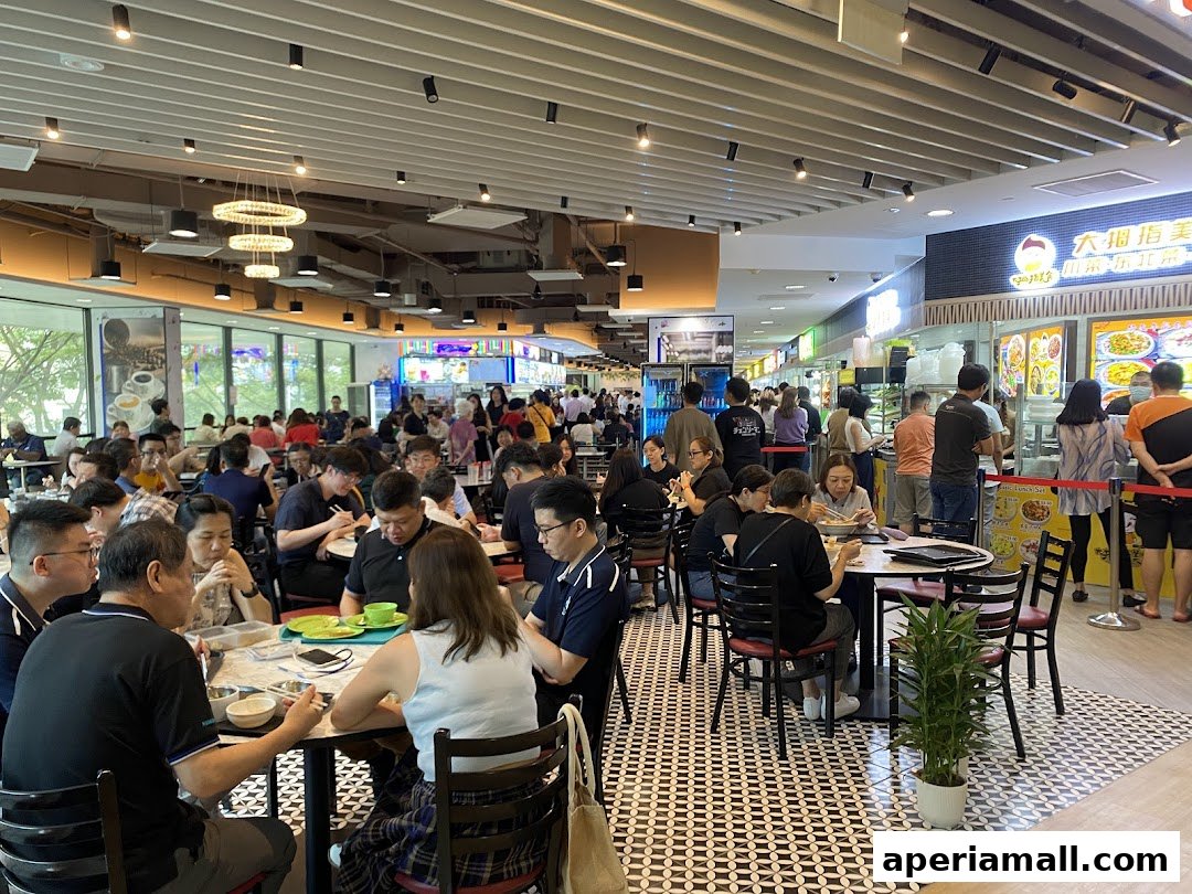 A busy food court with many people dining at tables and ordering food from stalls.