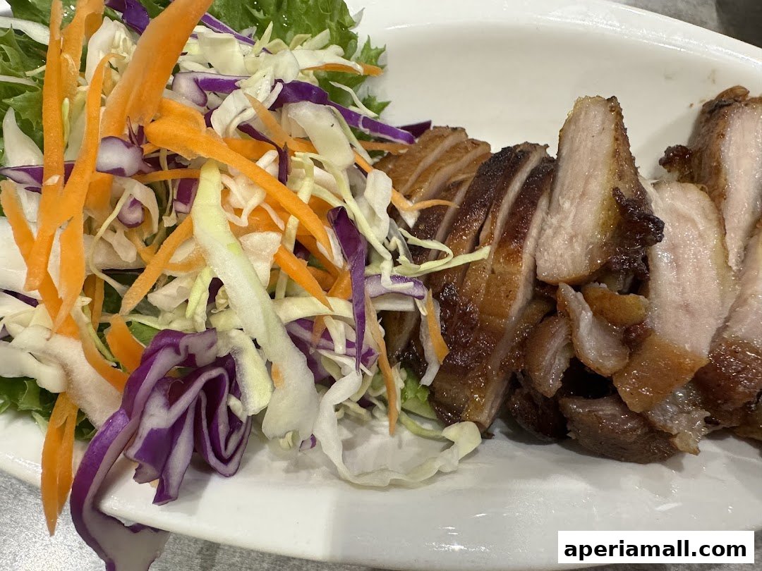 A plate of sliced grilled pork served with a fresh salad of lettuce, shredded carrots, and red cabbage.