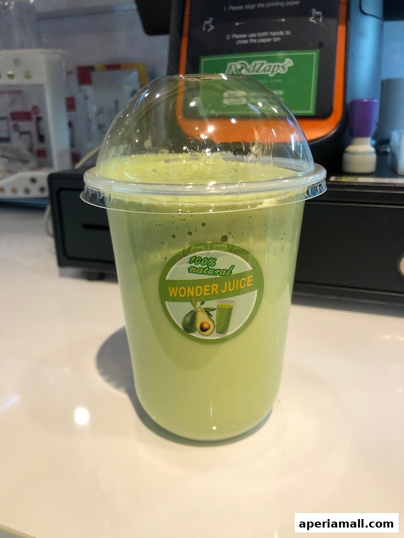 A close-up of a green smoothie in a clear plastic cup with a domed lid.