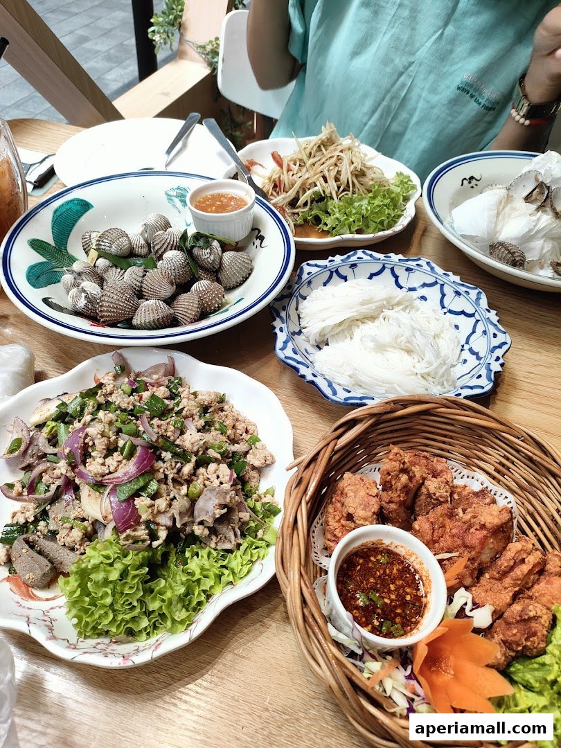 A table laden with various Thai dishes, including cockles, papaya salad, minced meat salad, and fried chicken.