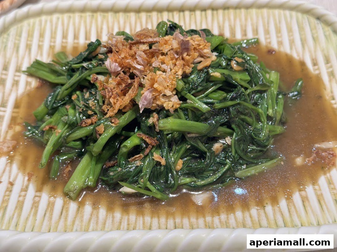 A close-up shot of stir-fried water spinach with fried garlic and a savory sauce.