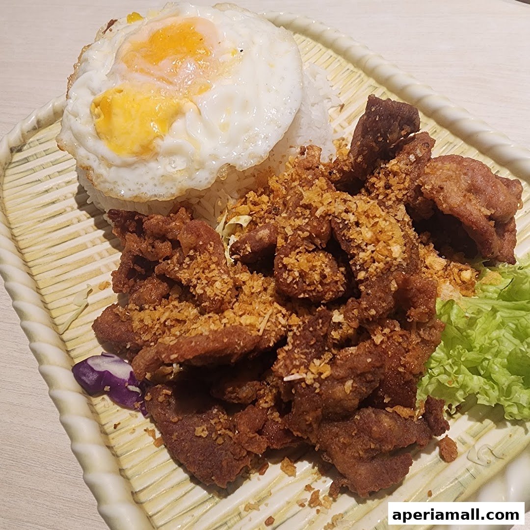 A plate of Thai food featuring crispy fried pork, rice, and a fried egg.