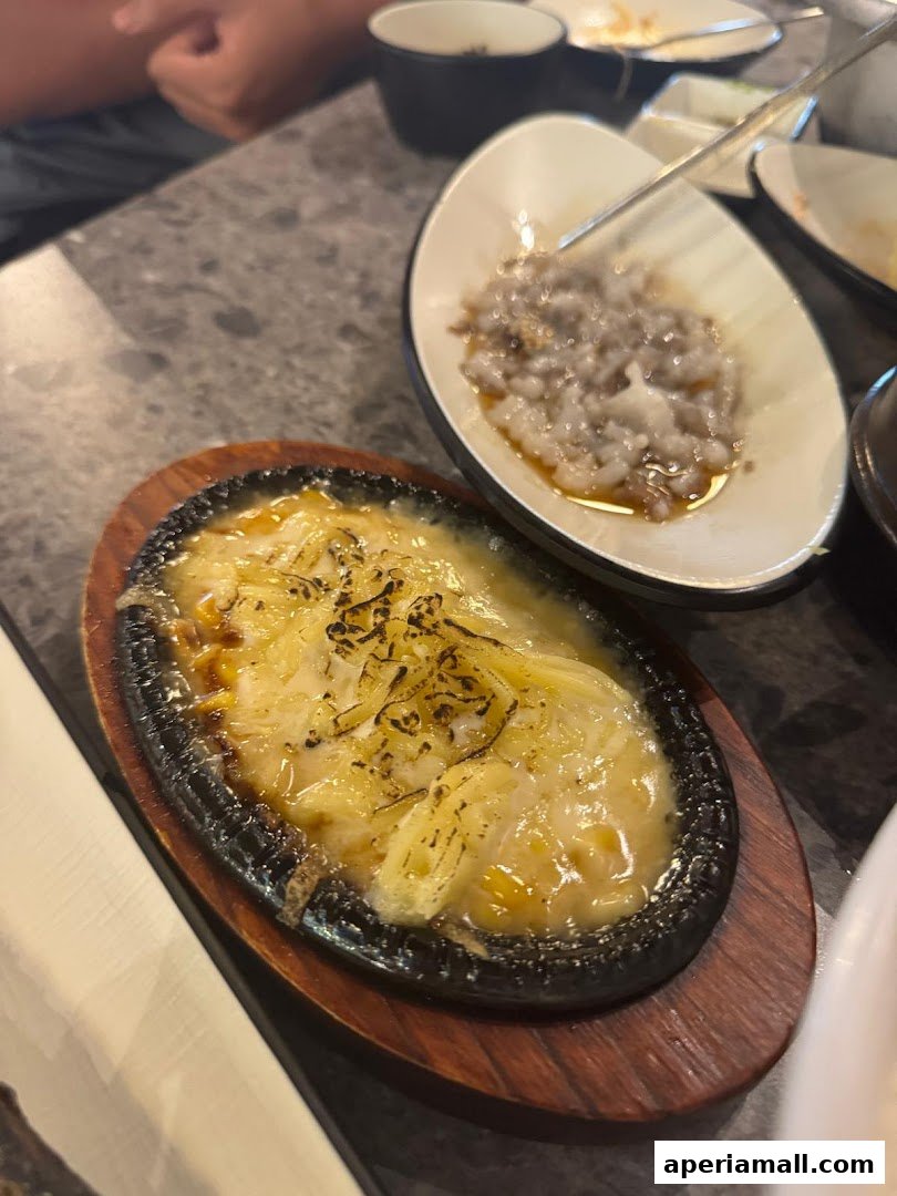 A sizzling dish with melted cheese and a side of seafood is served on a table.