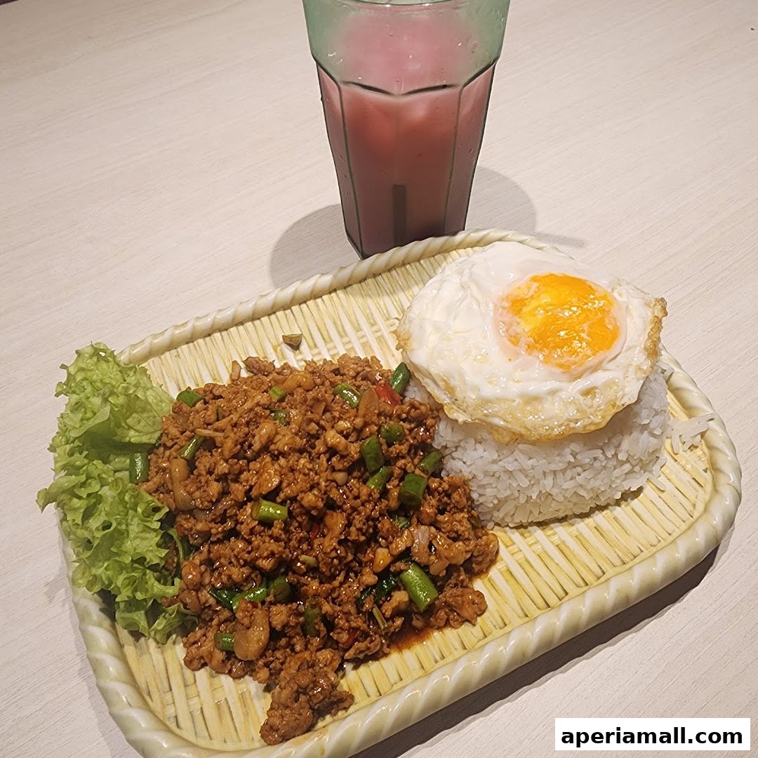 A plate of Thai basil minced meat with rice and a fried egg, served with a drink.
