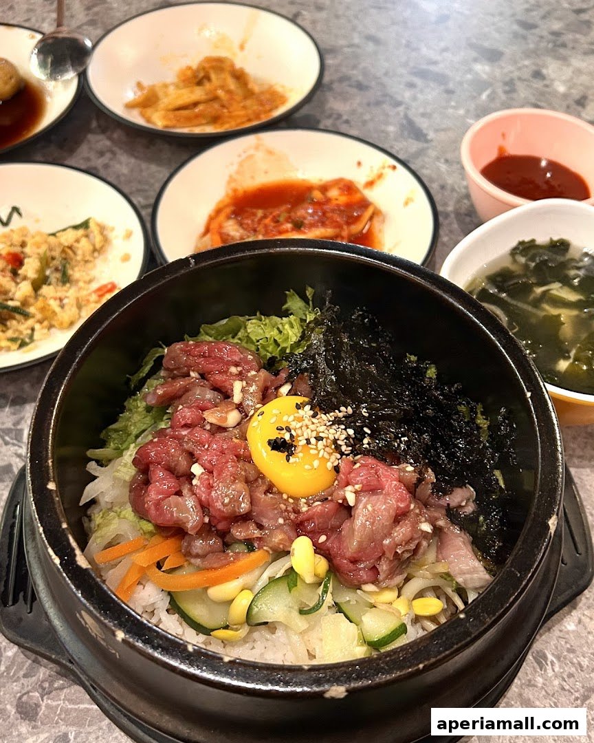 A close-up of a Korean dish with raw beef, egg yolk, vegetables, and rice in a stone bowl.