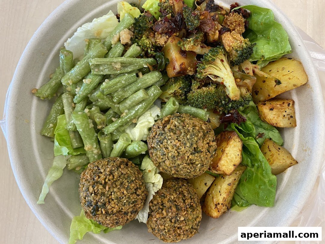A healthy salad bowl with falafel, green beans, roasted potatoes, and broccoli.