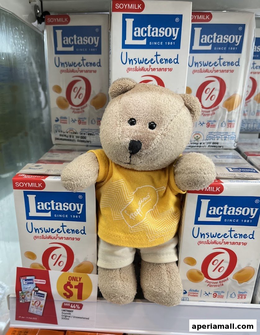 A teddy bear wearing a yellow shirt stands in front of Lactasoy Unsweetened soy milk cartons.