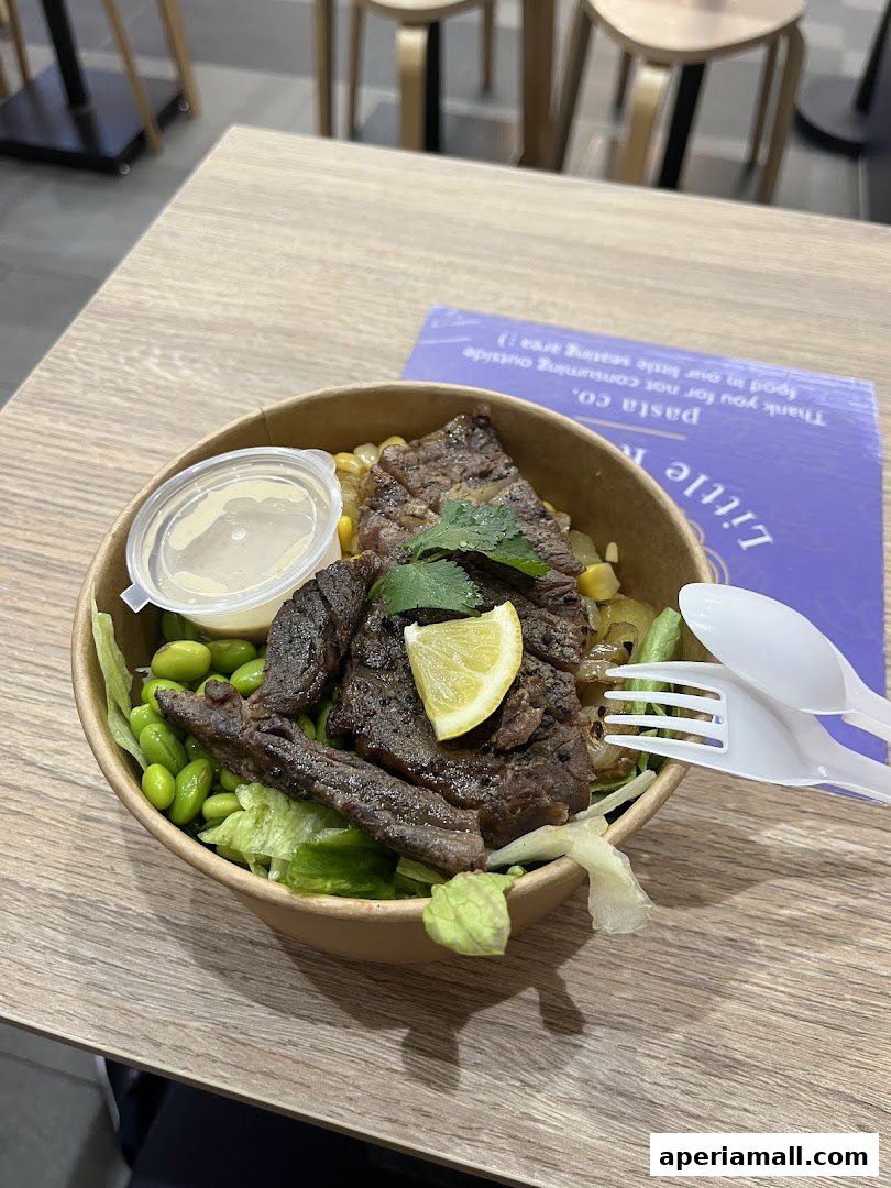 A healthy salad bowl with steak, edamame, corn, and a lemon wedge.