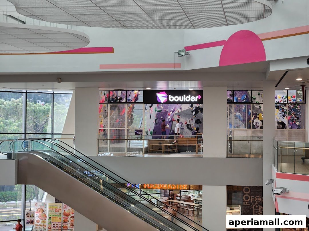 Interior view of a shopping mall featuring a bouldering gym and escalators.