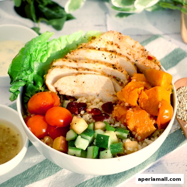 A close-up of a healthy salad bowl with grilled chicken, quinoa, pumpkin, tomatoes, and cucumber.