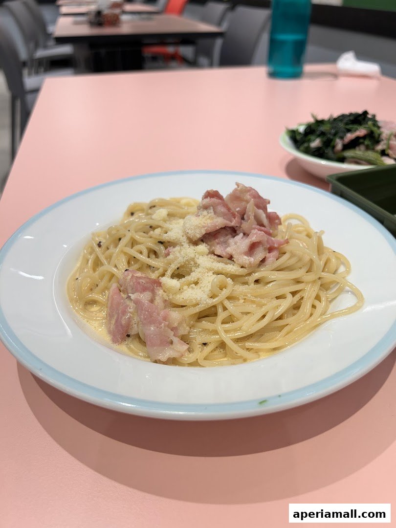 A plate of spaghetti carbonara with bacon and cheese on a pink table.