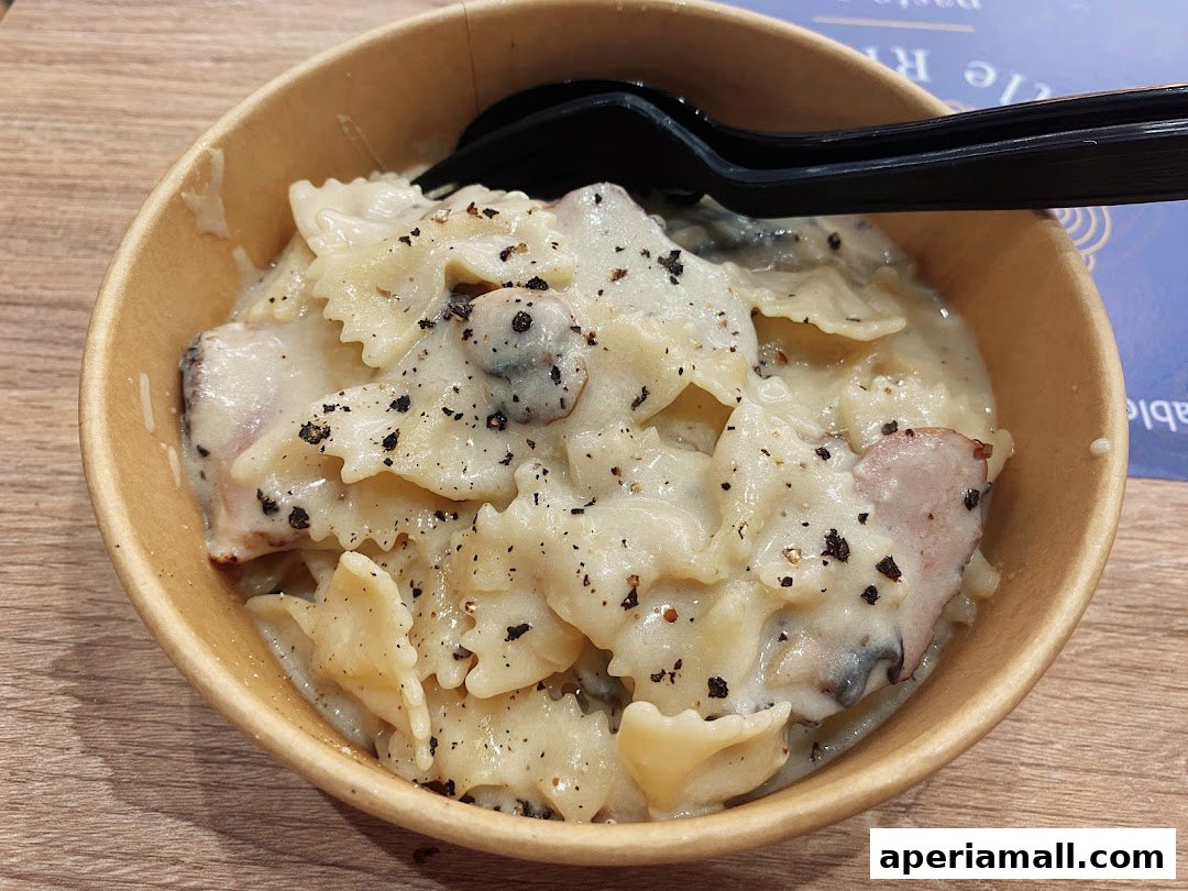 A close-up of a bowl of creamy pasta with ham and mushrooms, topped with black pepper.