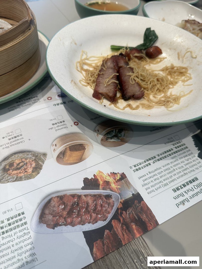 A table setting with a plate of noodles and char siu, and a menu with food images.