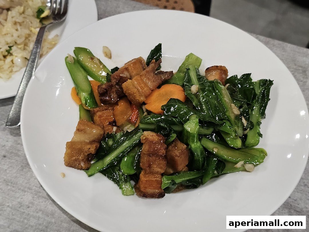 A plate of stir-fried vegetables with crispy pork and carrots, served with a side of fried rice.