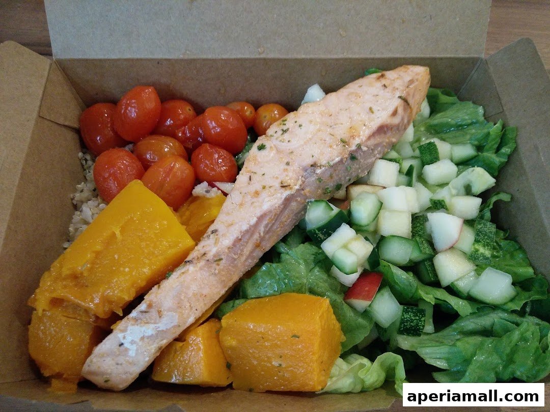 A healthy meal box with salmon, pumpkin, cherry tomatoes, cucumber, and lettuce.