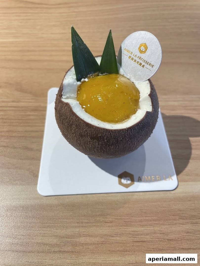 A close-up of a dessert shaped like a coconut, topped with mango and green leaves.