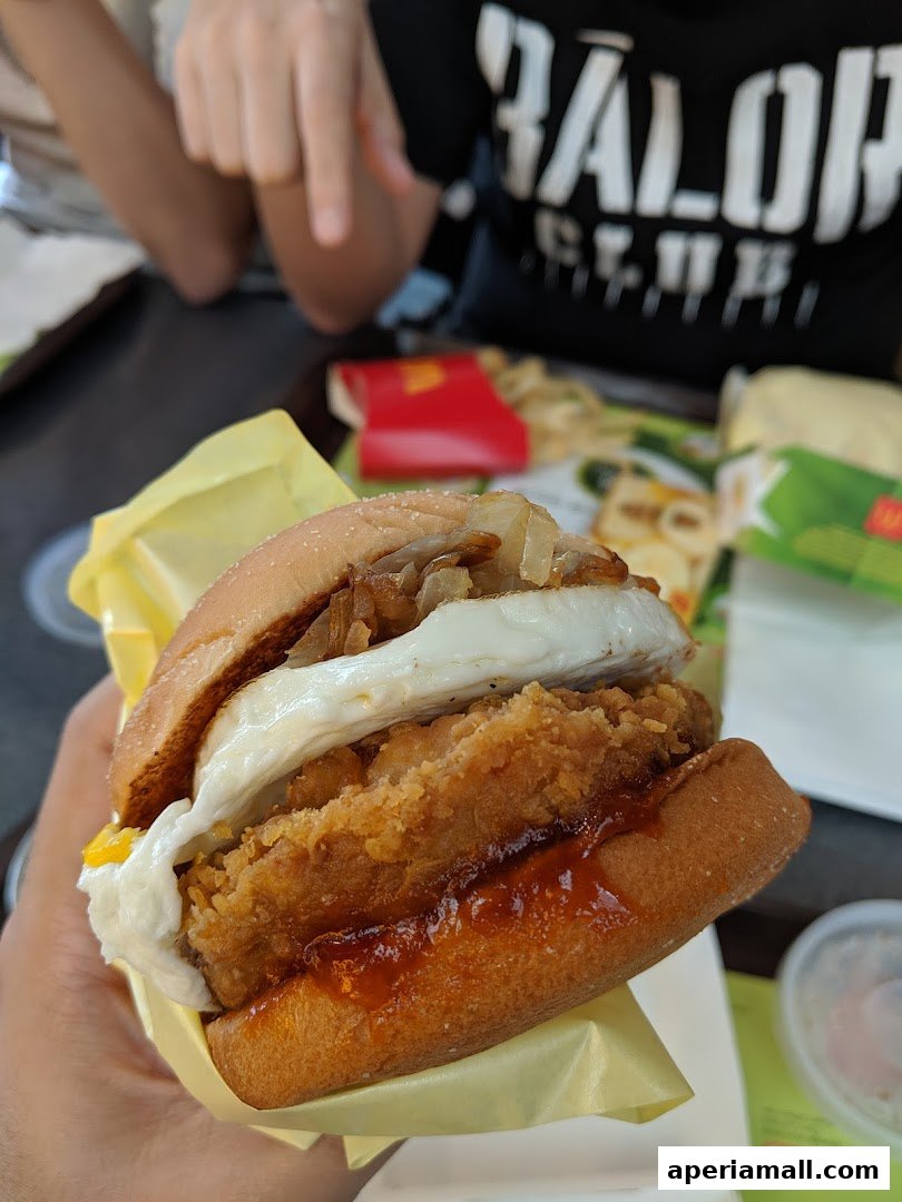 A hand holds a delicious McDonald's burger with fried chicken, egg, and onions.