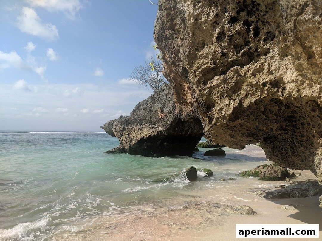 A serene beach scene with turquoise water, sandy shore, and large rock formations.