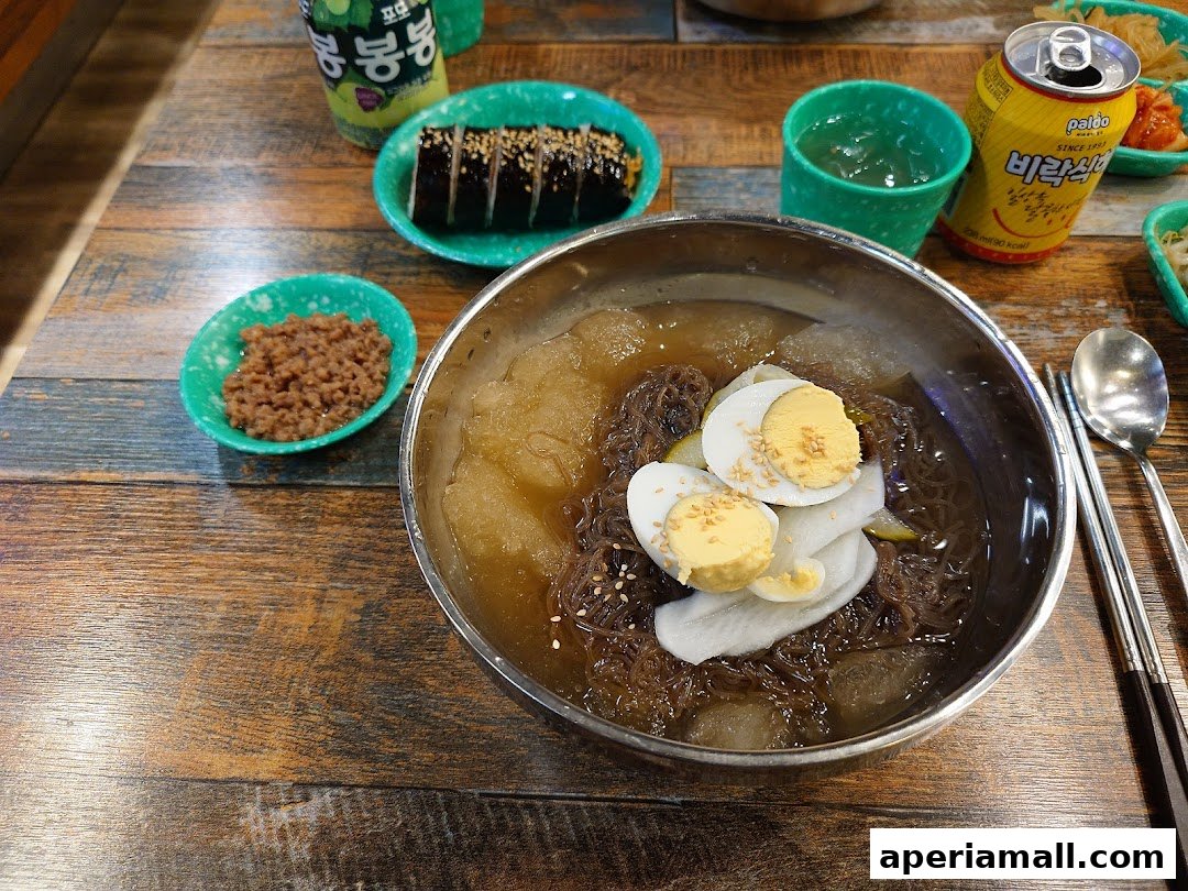 A close-up of a delicious Korean cold noodle dish with side dishes and drinks.
