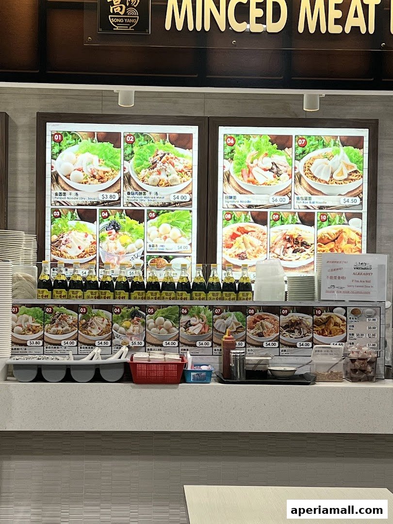 A food stall display featuring various noodle dishes with prices and images.