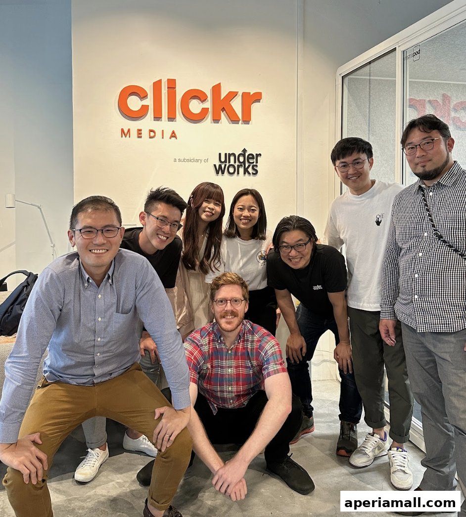 A diverse team of eight people posing for a photo in front of the Clickr Media logo.