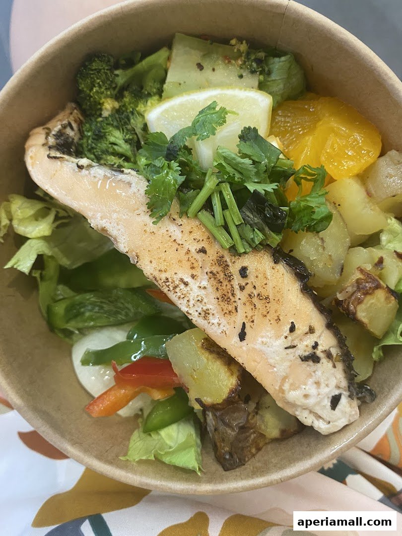 A close-up of a healthy salad bowl with grilled salmon, broccoli, potatoes, and citrus.