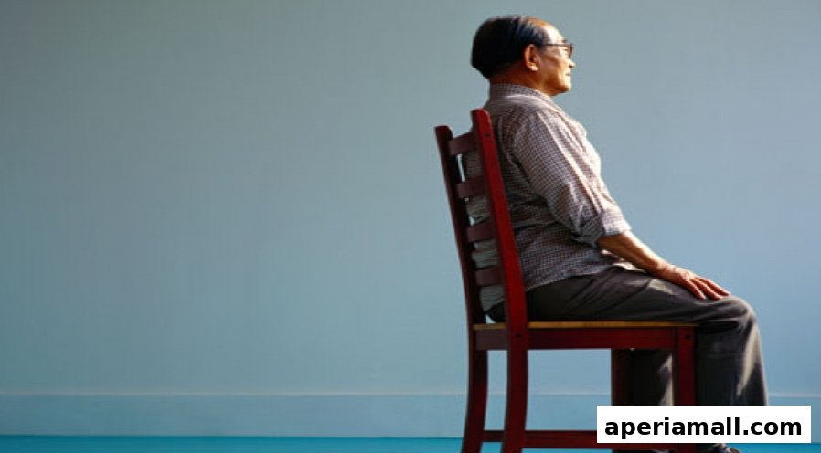 An elderly man sits on a wooden chair, looking to the side against a light blue background.