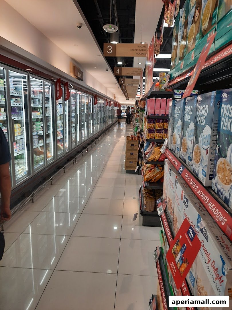 Aisle in a supermarket with refrigerated displays and shelves stocked with cereals and other products.
