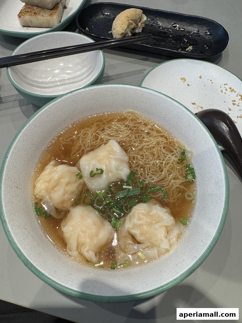 A close-up shot of a bowl of wonton noodle soup with chopsticks and other dishes in the background.