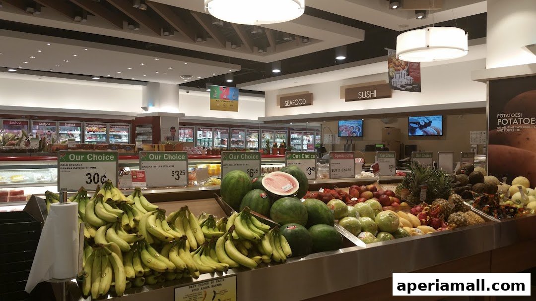 A grocery store aisle featuring fresh produce, including bananas, watermelons, and other fruits, with signage for seafood and sushi.