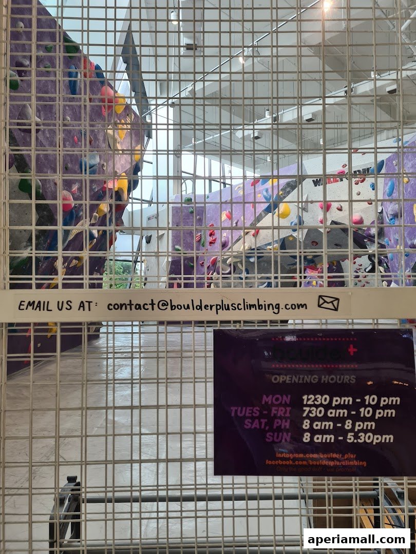 Interior view of a climbing gym with colorful holds on purple walls, seen through a metal grid.