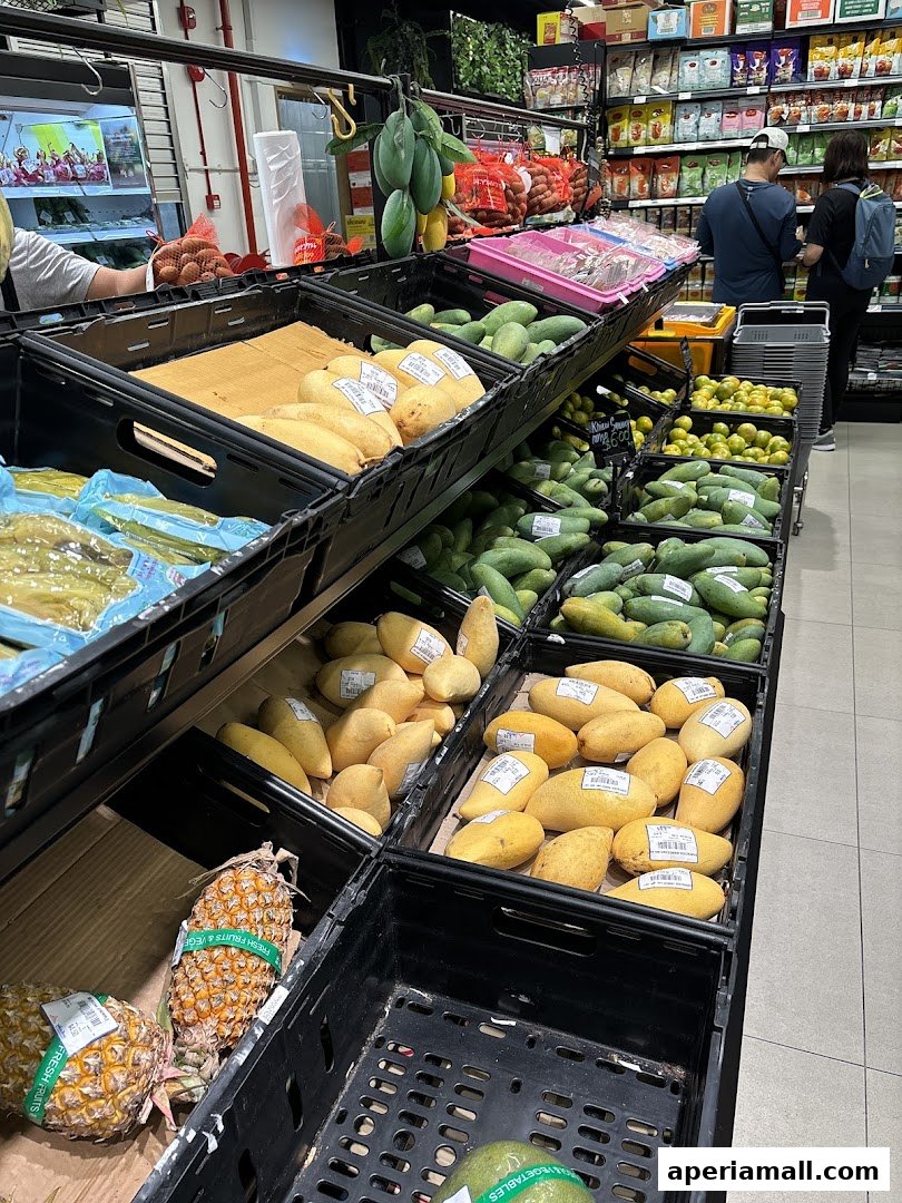 Aisle of fresh fruits and vegetables in a supermarket, with mangoes and pineapples prominently displayed.