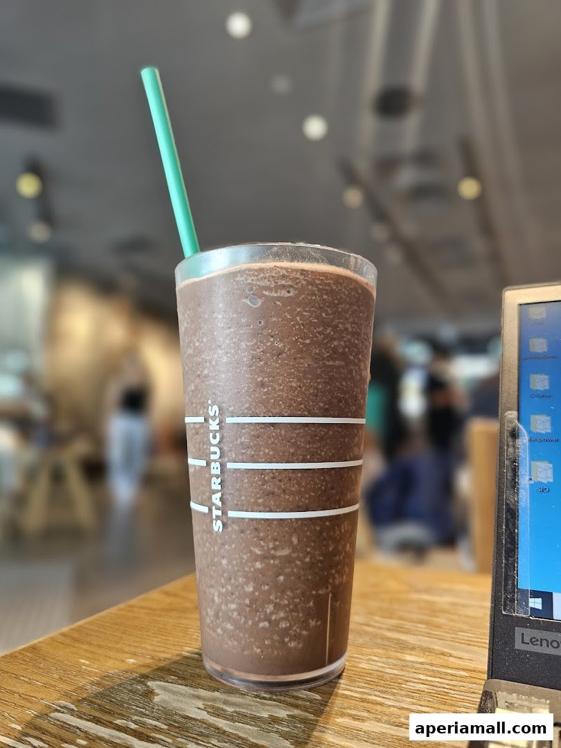 A close-up of a Starbucks Frappuccino with a green straw on a wooden table.