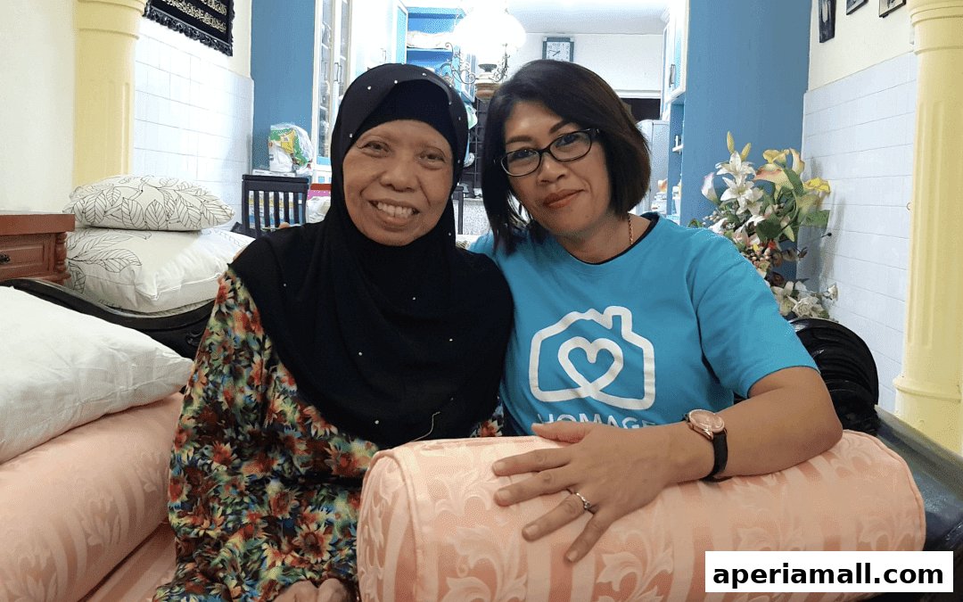 Two women smiling, one wearing a hijab and the other a blue t-shirt with a house and heart logo.
