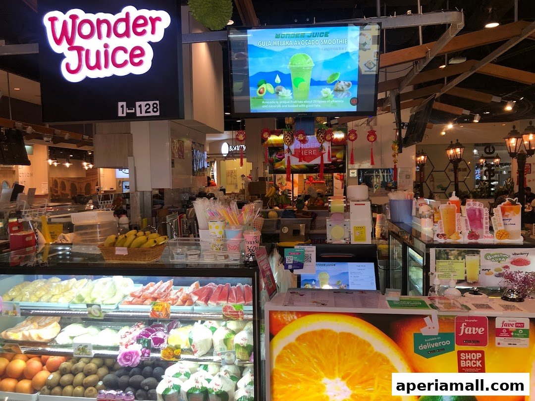 A brightly lit juice shop counter displaying fresh fruits and promotional materials.