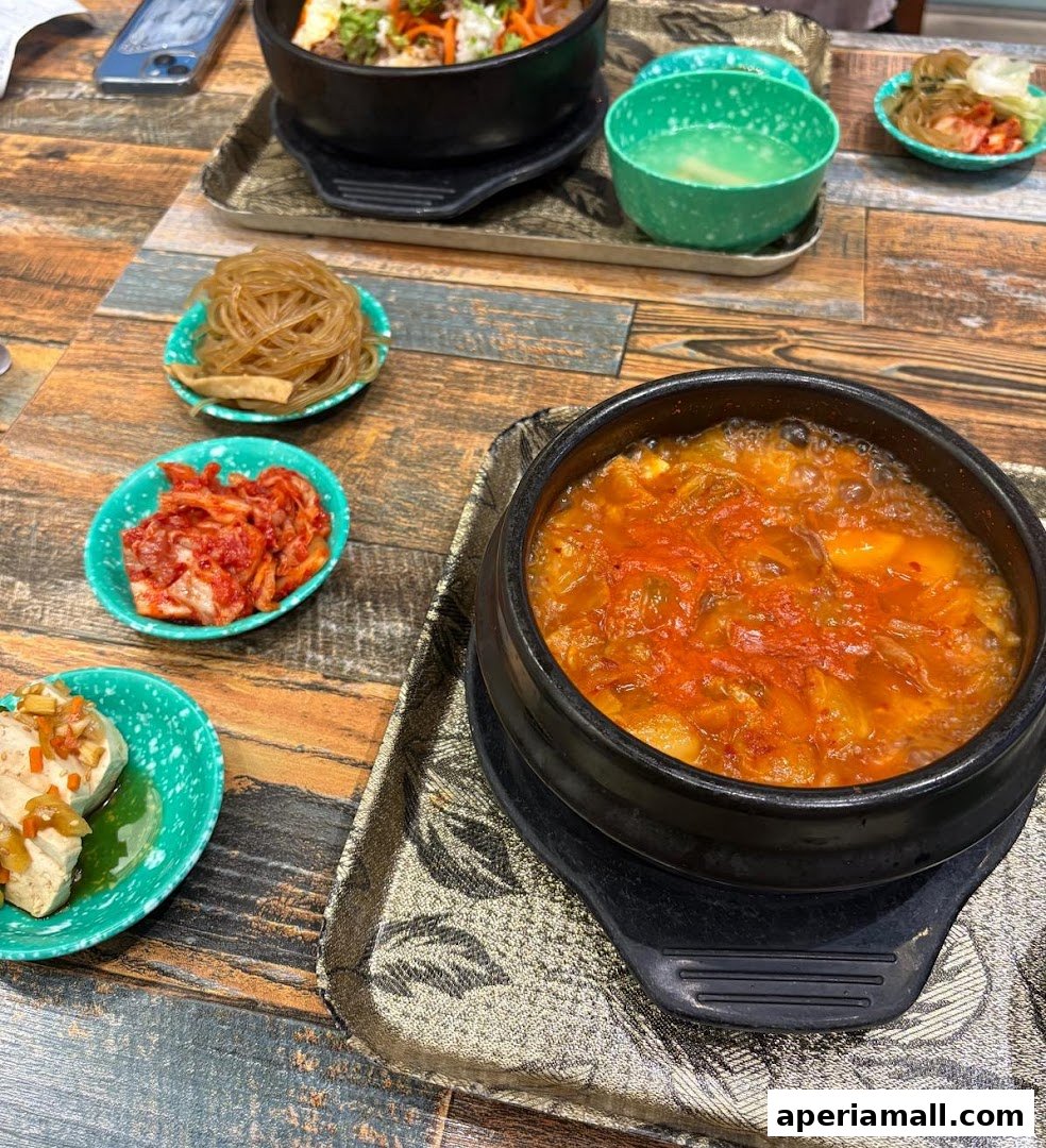 A table laden with Korean dishes, including a bubbling stew, kimchi, and noodles.