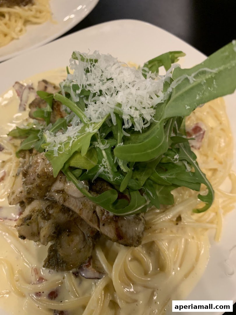 A close-up of a creamy pasta dish topped with grilled chicken, arugula, and grated cheese.