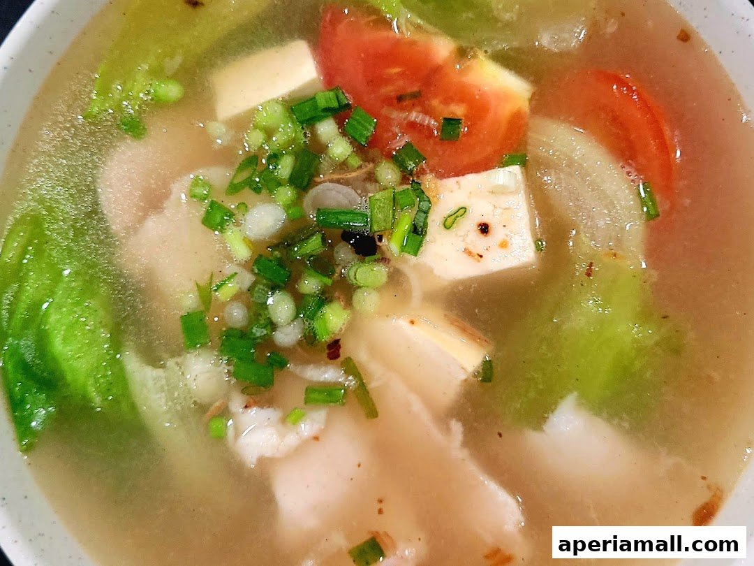 A close-up shot of a steaming bowl of soup with fish, tofu, tomatoes, and green onions.