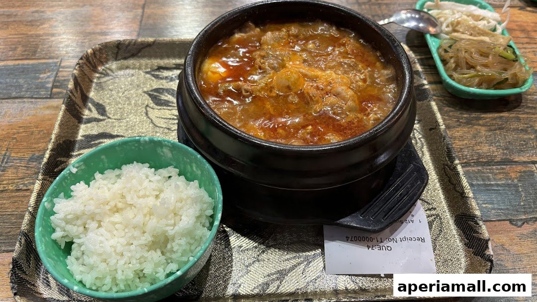 A steaming bowl of Korean stew with rice and side dishes on a textured tray.