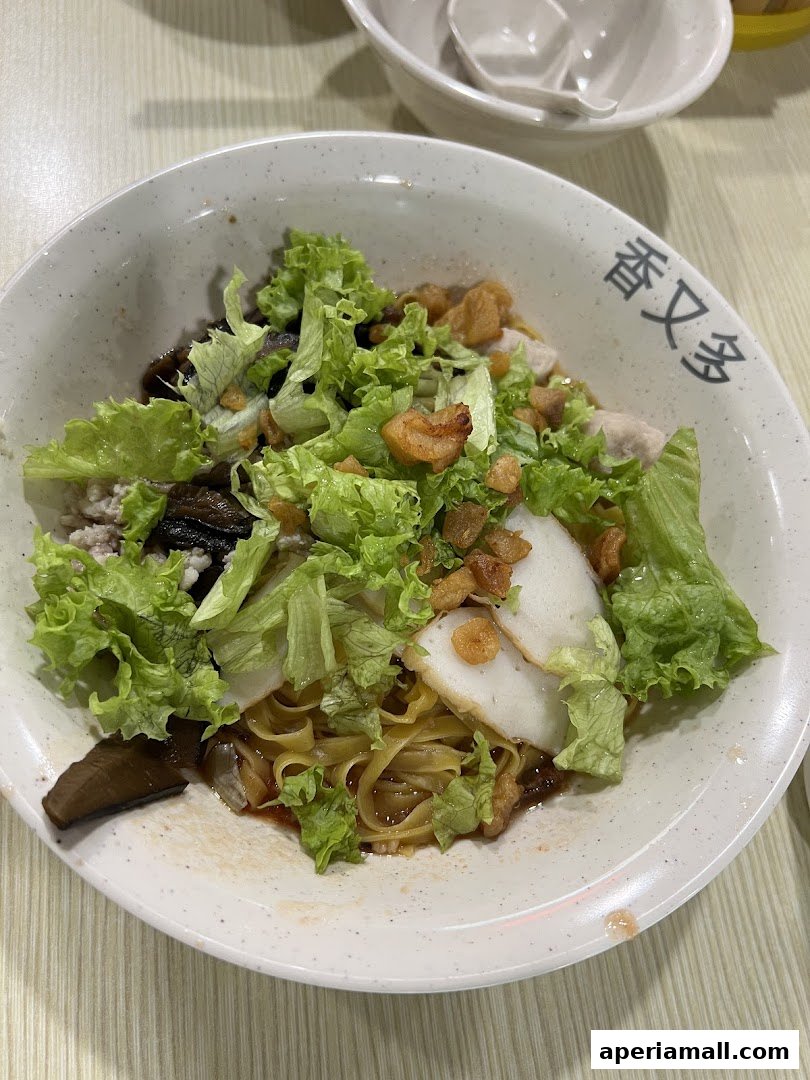 A close-up of a delicious bowl of noodles with fresh lettuce, mushrooms, and fish cakes.