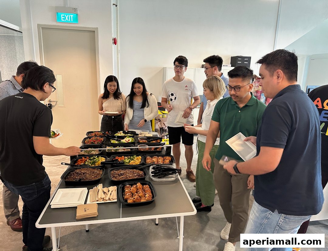 People gathering around a table filled with various catered food containers.