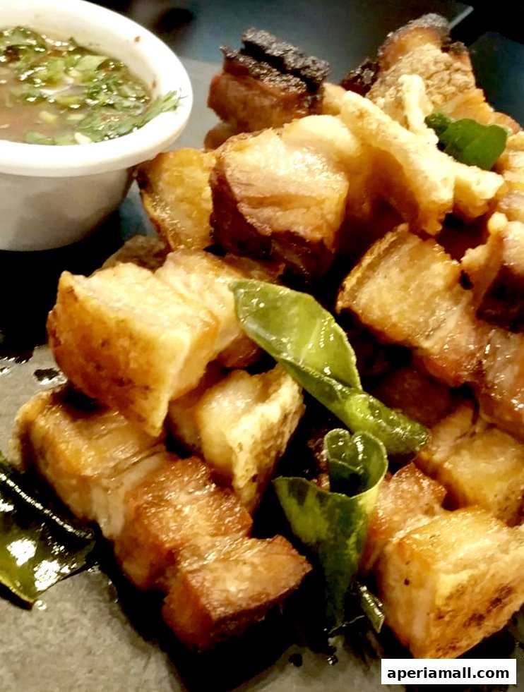Crispy pork belly bites served with a dipping sauce and garnished with herbs.