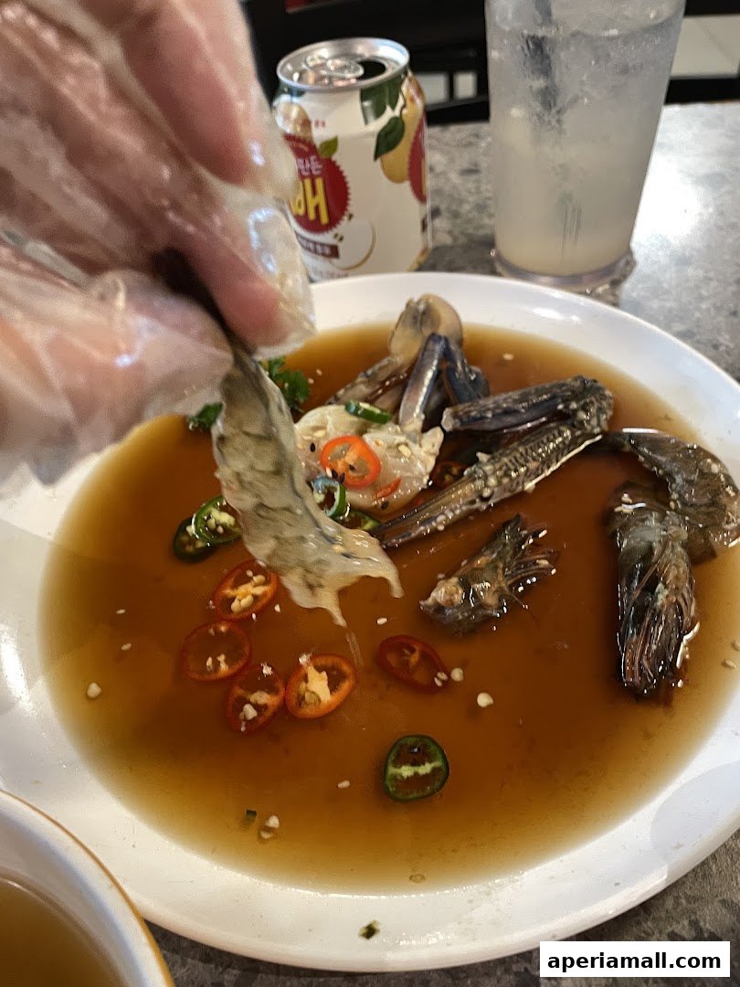 A person in gloves picks up marinated seafood from a plate with chili peppers and sauce.