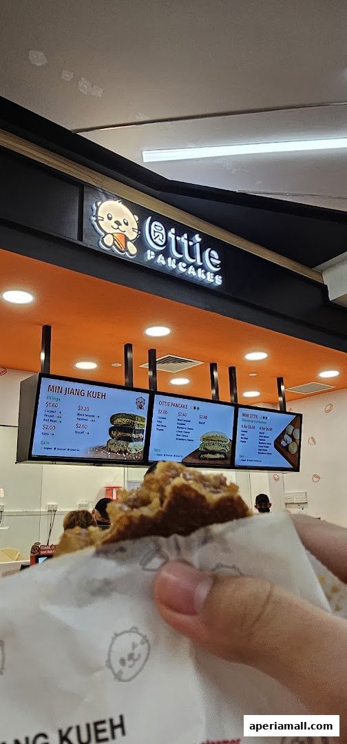 A person holds a delicious pancake from Ottie Pancakes, with the shop's menu displayed behind.