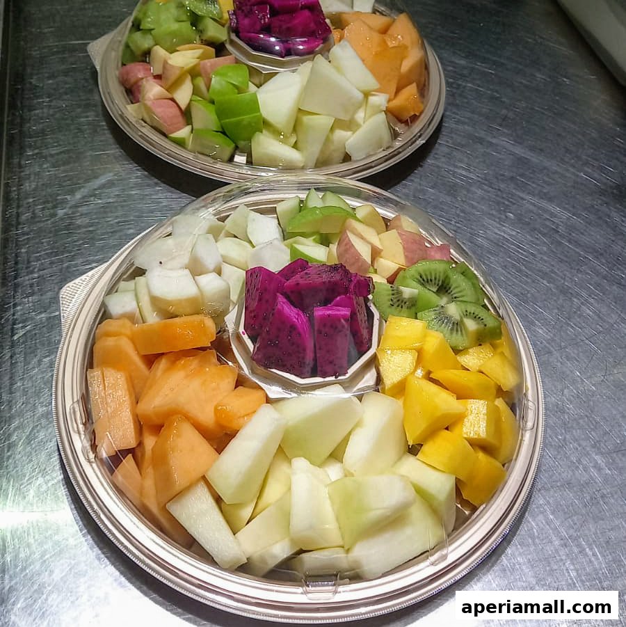 Two platters of freshly cut, colorful fruits including dragon fruit, kiwi, melon, and apples.