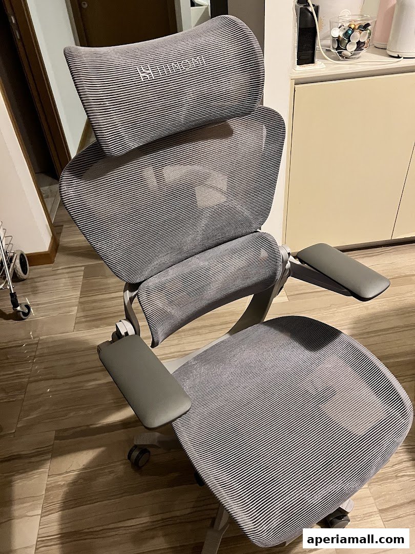 A grey ergonomic chair with adjustable headrest and armrests, branded 'Hinomi'.