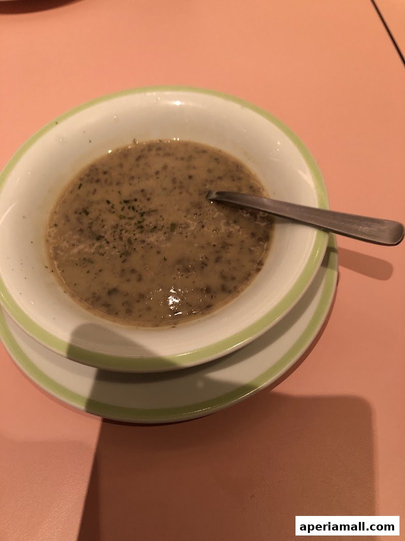 A bowl of creamy mushroom soup with a spoon rests on a pink table.