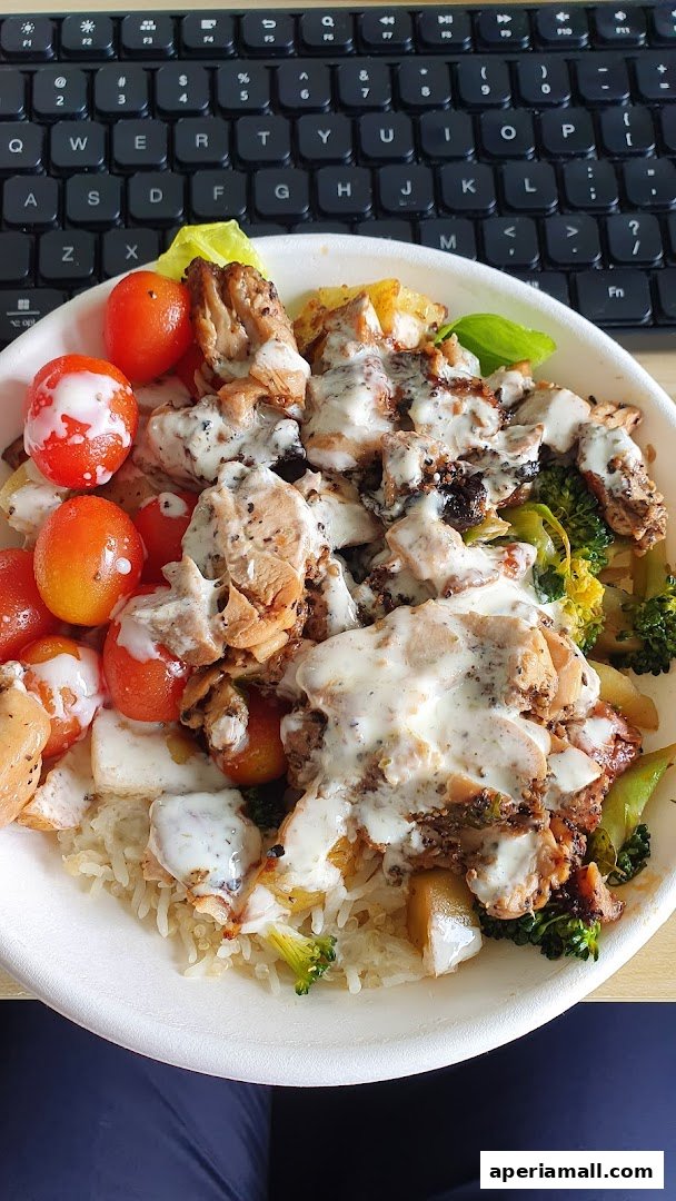 A healthy salad bowl with grilled chicken, cherry tomatoes, broccoli, and rice, drizzled with sauce.
