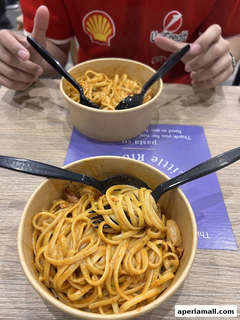 Two bowls of pasta with forks and spoons on a wooden table.