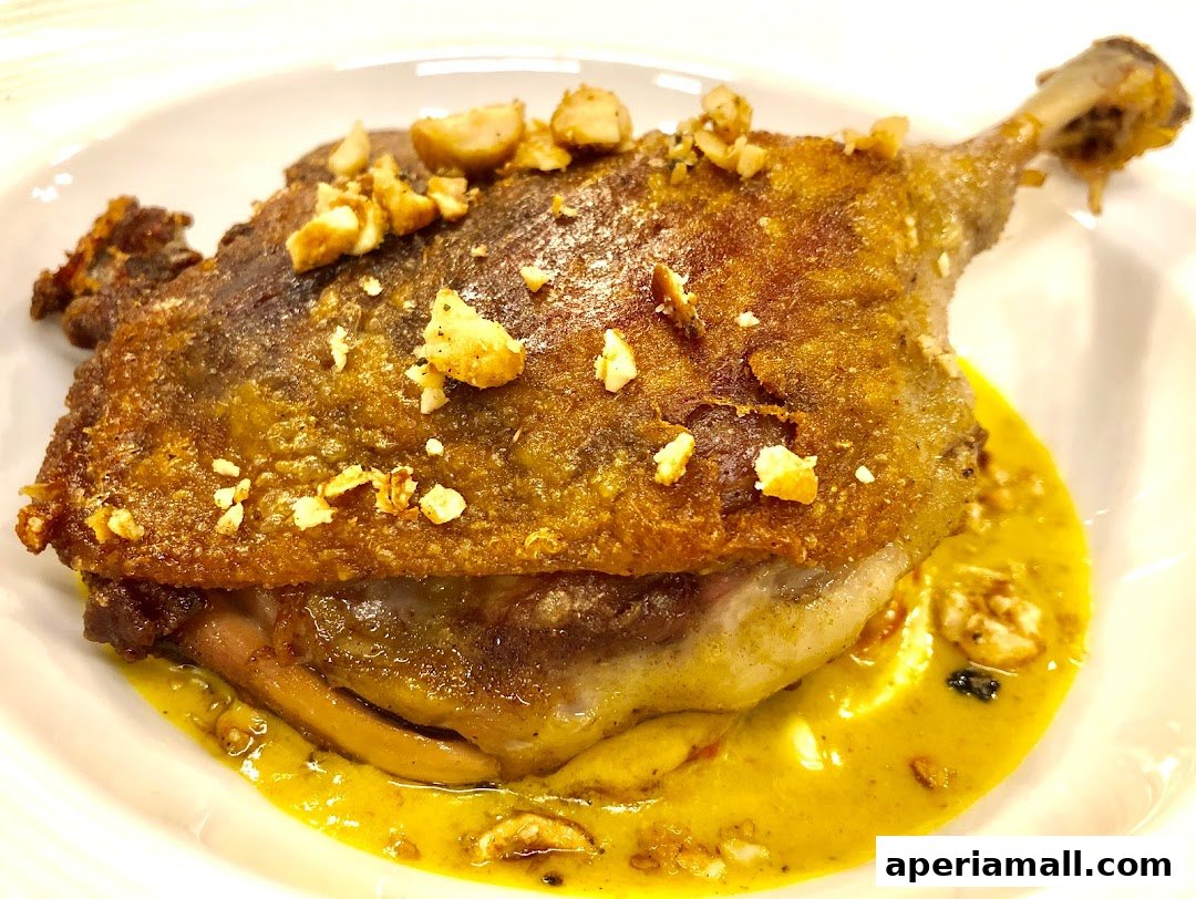 A close-up of a crispy duck leg dish with a rich sauce and chopped nuts.